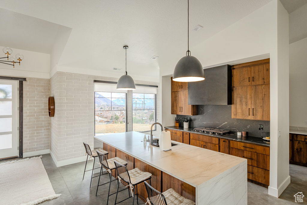 Kitchen with a center island with sink, tile floors, hanging light fixtures, a breakfast bar, and tasteful backsplash
