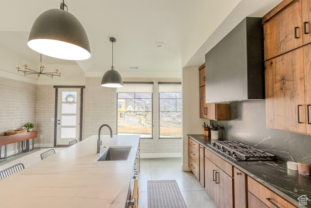 Kitchen featuring stainless steel gas cooktop, decorative light fixtures, light tile flooring, a notable chandelier, and wall chimney range hood