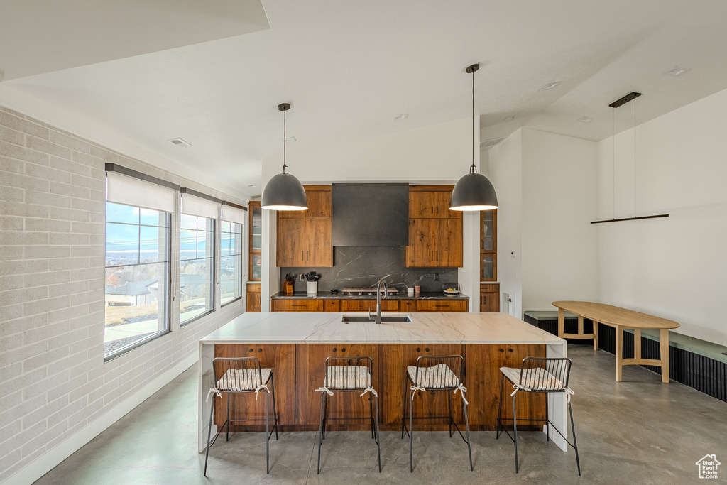 Kitchen featuring pendant lighting, lofted ceiling, a kitchen island with sink, and range hood