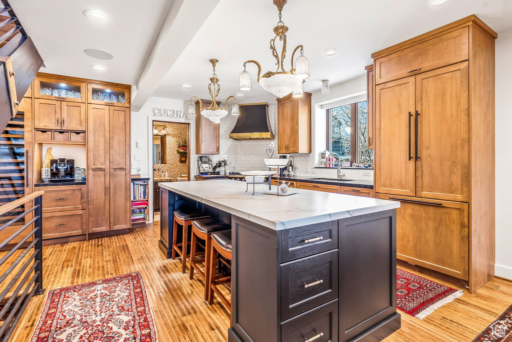 Kitchen featuring a center island, sink, premium range hood, an inviting chandelier, and light stone countertops