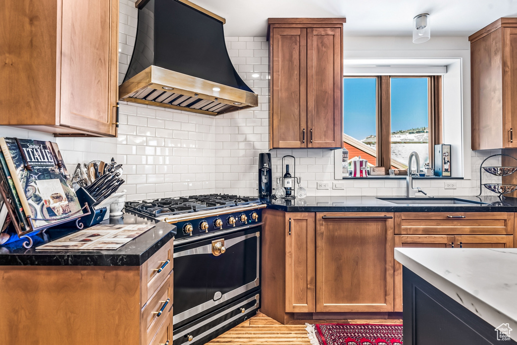 Kitchen featuring wall chimney exhaust hood, tasteful backsplash, stainless steel range with gas stovetop, and sink