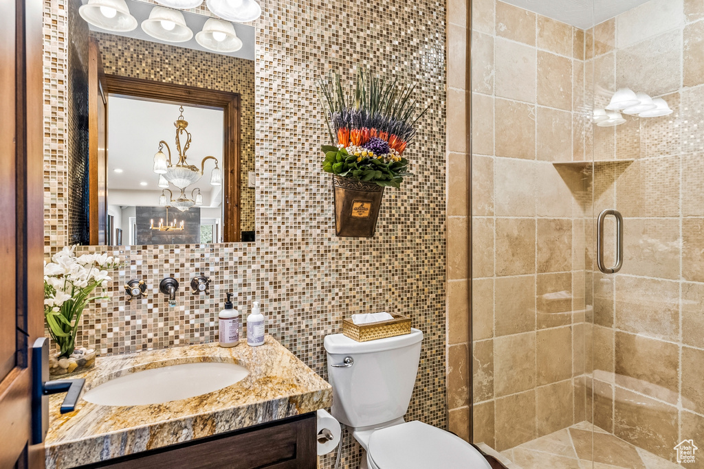 Bathroom with tasteful backsplash, tile walls, walk in shower, toilet, and vanity with extensive cabinet space