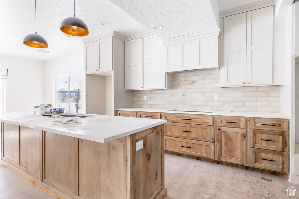 Kitchen featuring hanging light fixtures, light stone countertops, white cabinetry, light colored carpet, and tasteful backsplash