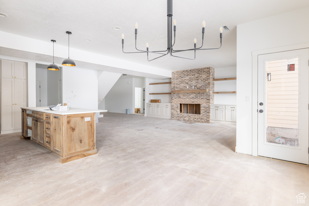 Kitchen with pendant lighting, a kitchen island with sink, an inviting chandelier, a fireplace, and brick wall