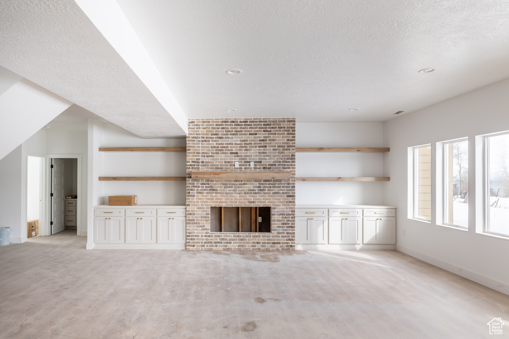 Unfurnished living room featuring a textured ceiling, brick wall, and a fireplace