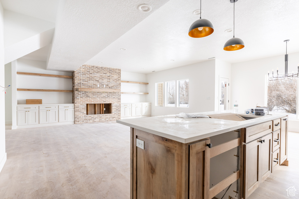 Kitchen with pendant lighting, light stone countertops, brick wall, a center island, and a brick fireplace