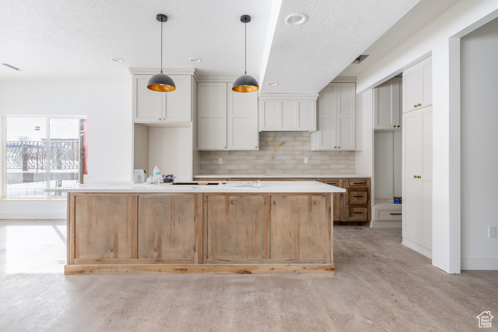 Kitchen featuring white cabinets, backsplash, a kitchen island, and pendant lighting