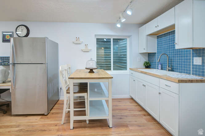 Kitchen featuring white cabinets, backsplash, stainless steel fridge, and light hardwood / wood-style flooring