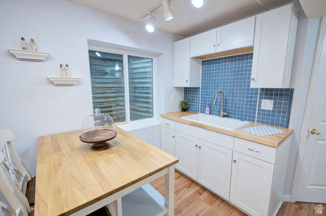 Kitchen featuring rail lighting, white cabinetry, sink, and light hardwood / wood-style flooring