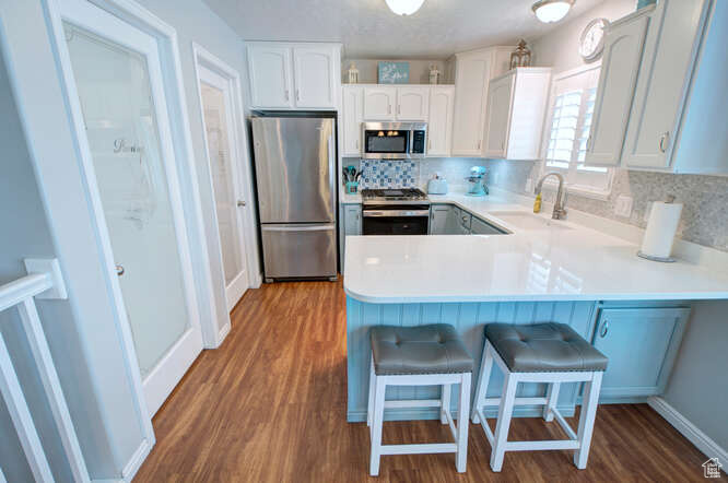 Kitchen featuring appliances with stainless steel finishes, tasteful backsplash, kitchen peninsula, and hardwood / wood-style flooring