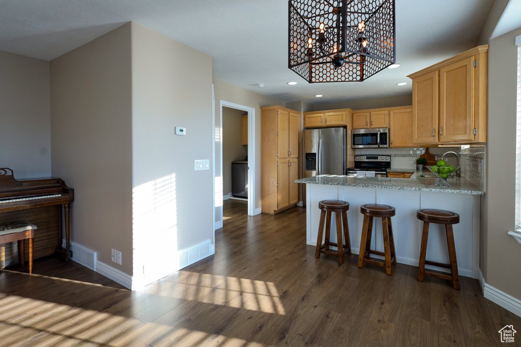 Kitchen featuring backsplash, kitchen peninsula, stainless steel appliances, dark hardwood / wood-style floors, and an inviting chandelier