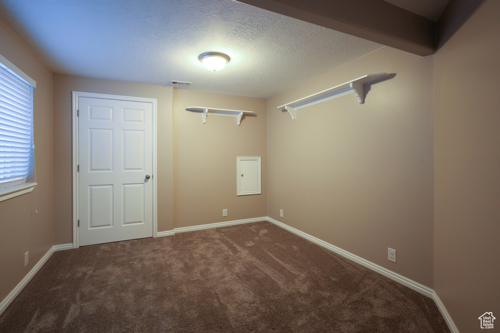 Unfurnished bedroom with a textured ceiling and dark colored carpet