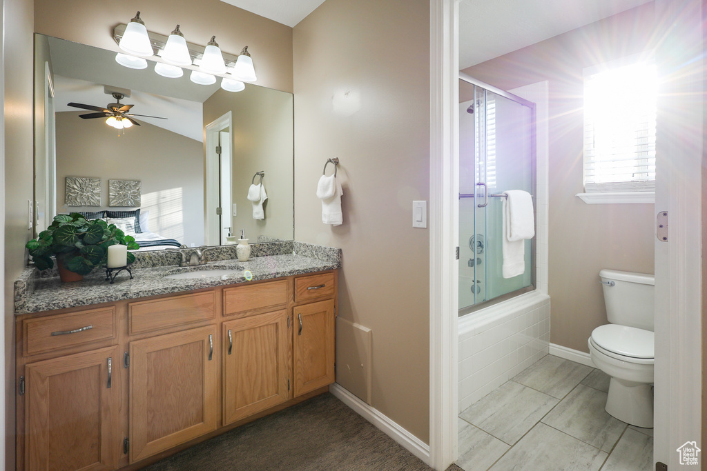 Full bathroom featuring vanity, tile flooring, ceiling fan, toilet, and combined bath / shower with glass door