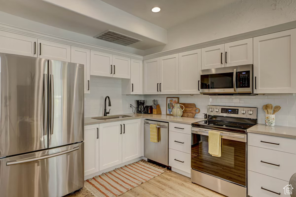 Kitchen featuring backsplash, stainless steel appliances, sink, white cabinetry, and light hardwood / wood-style flooring