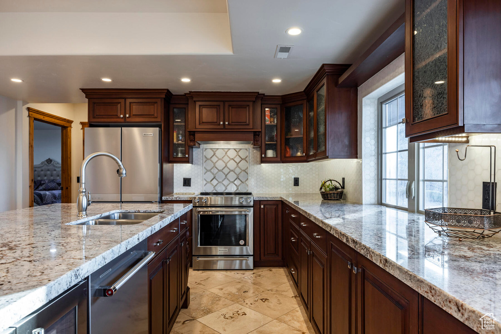 Kitchen featuring light stone counters, appliances with stainless steel finishes, sink, and backsplash