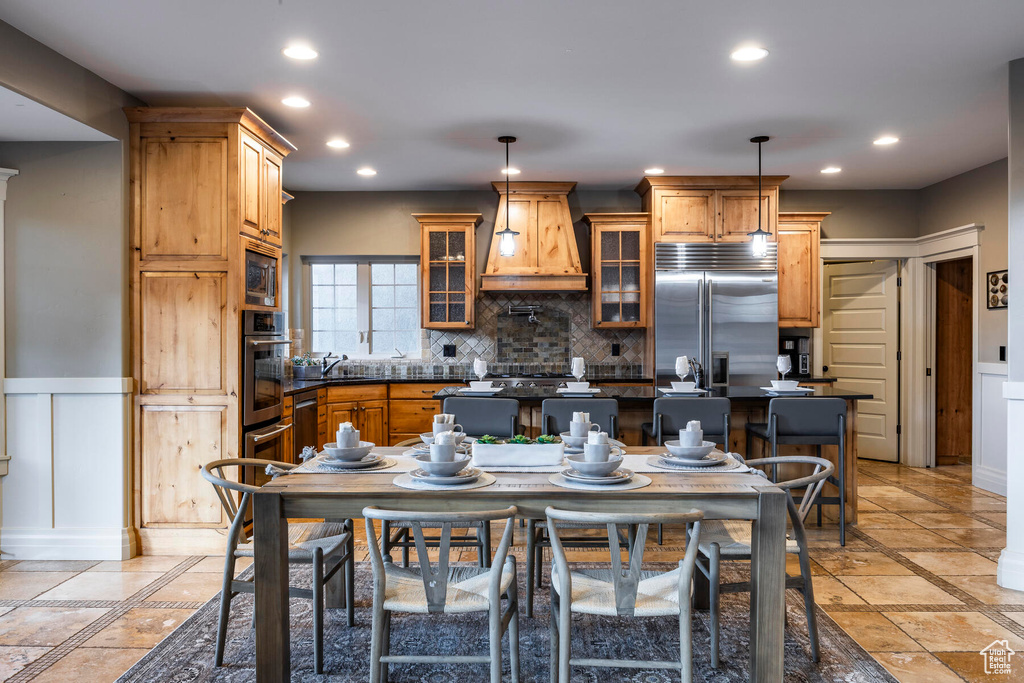 Kitchen featuring built in appliances, custom range hood, light tile floors, and decorative light fixtures