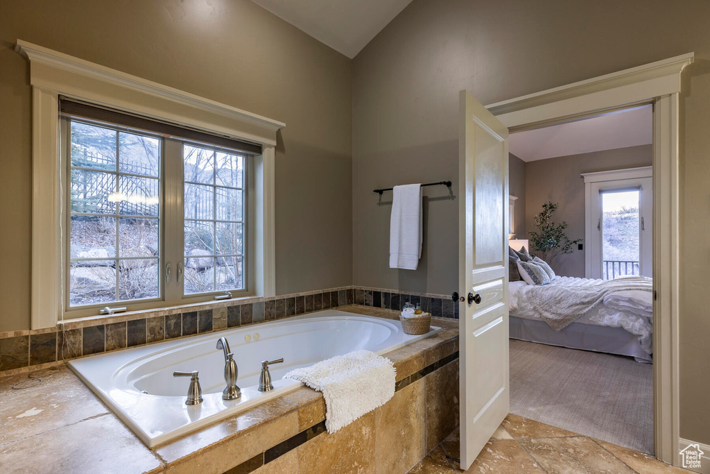 Bathroom featuring tiled bath, lofted ceiling, and tile flooring