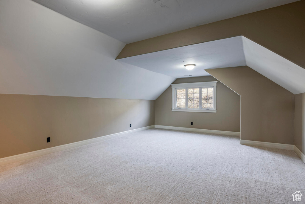 Additional living space with light colored carpet and vaulted ceiling