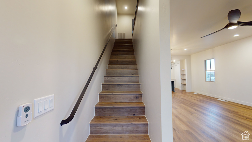 Stairs with wood-type flooring and ceiling fan with notable chandelier