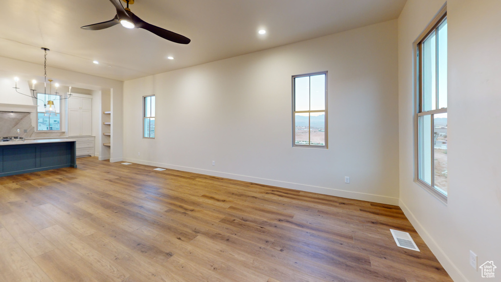 Unfurnished living room with ceiling fan with notable chandelier and light wood-type flooring