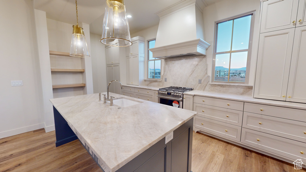 Kitchen featuring light hardwood / wood-style flooring, high end stainless steel range, decorative light fixtures, sink, and premium range hood