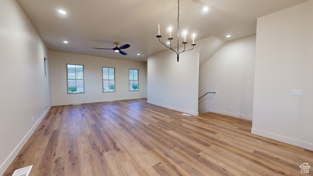 Unfurnished living room with ceiling fan with notable chandelier and light hardwood / wood-style floors