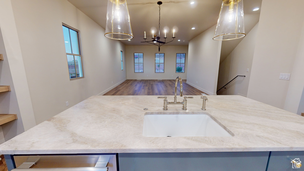 Kitchen featuring an island with sink, light stone countertops, hardwood / wood-style flooring, sink, and pendant lighting