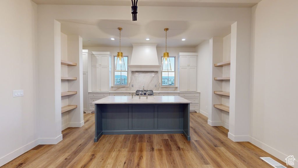 Kitchen with built in features, light hardwood / wood-style floors, decorative light fixtures, custom exhaust hood, and white cabinets