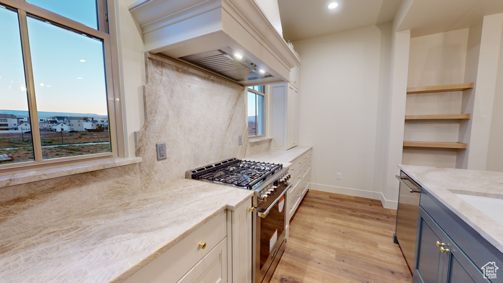 Kitchen featuring light stone counters, stainless steel appliances, light wood-type flooring, and custom range hood