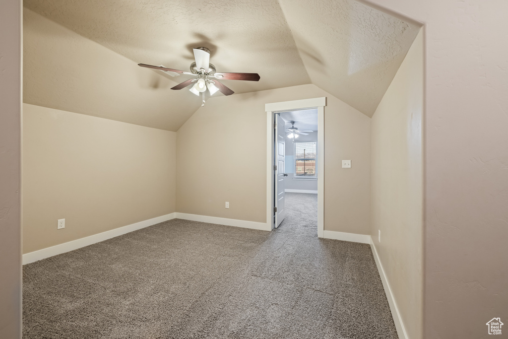 Additional living space with dark carpet, ceiling fan, lofted ceiling, and a textured ceiling