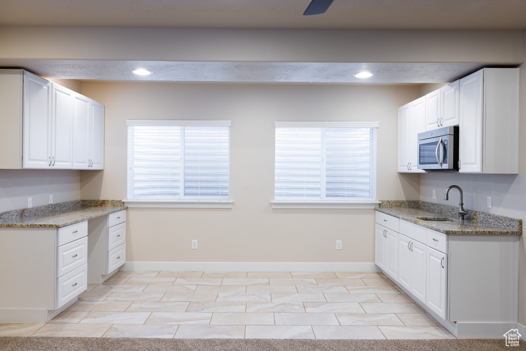 Kitchen with white cabinets, light stone counters, ceiling fan, and light tile floors