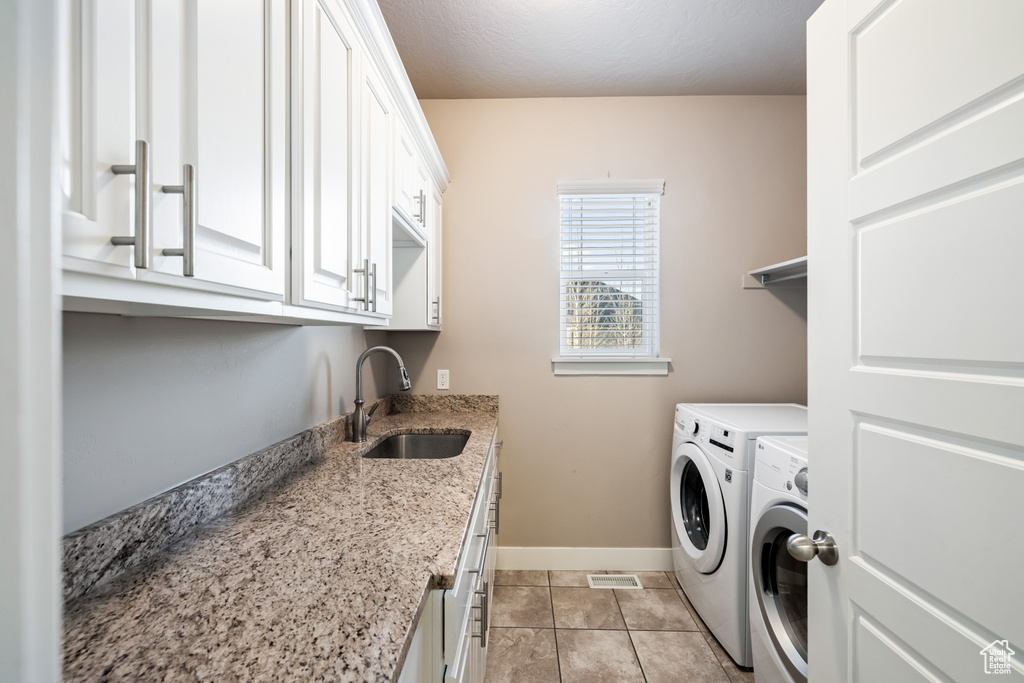 Clothes washing area with washing machine and dryer, cabinets, sink, and light tile floors
