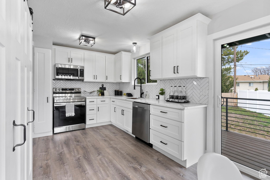 Kitchen with stainless steel appliances, sink, tasteful backsplash, white cabinetry, and light hardwood / wood-style floors