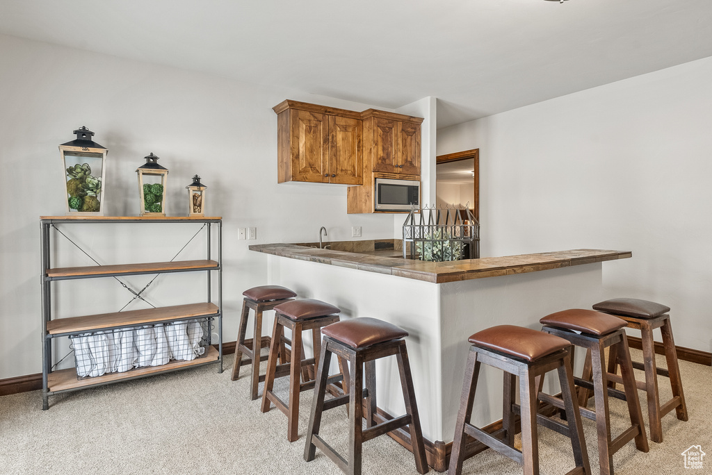 Kitchen with a breakfast bar, light carpet, kitchen peninsula, and stainless steel microwave