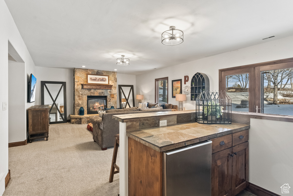 Kitchen featuring a stone fireplace, light carpet, dark brown cabinetry, and refrigerator