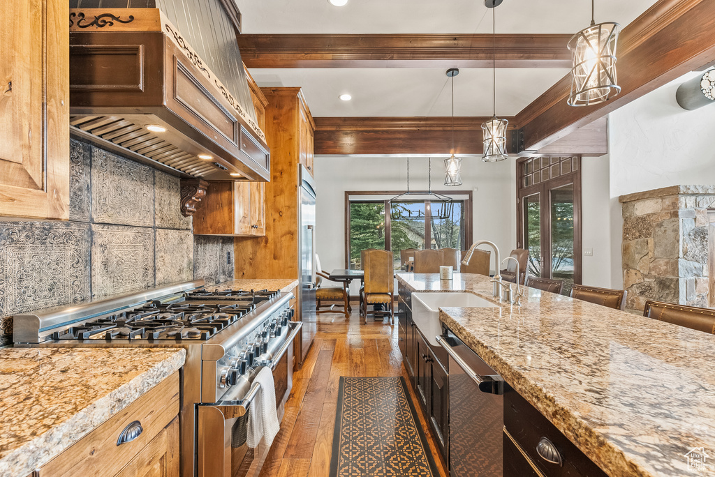 Kitchen featuring backsplash, decorative light fixtures, premium range hood, premium appliances, and dark hardwood / wood-style flooring