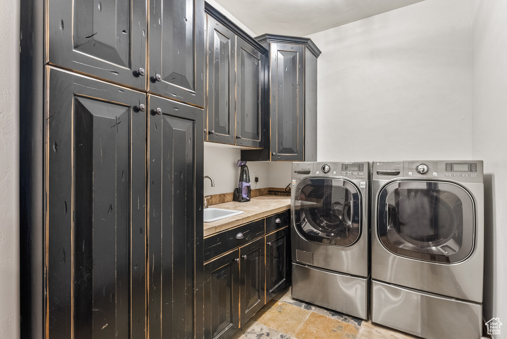 Clothes washing area featuring cabinets, sink, washing machine and dryer, and light tile flooring
