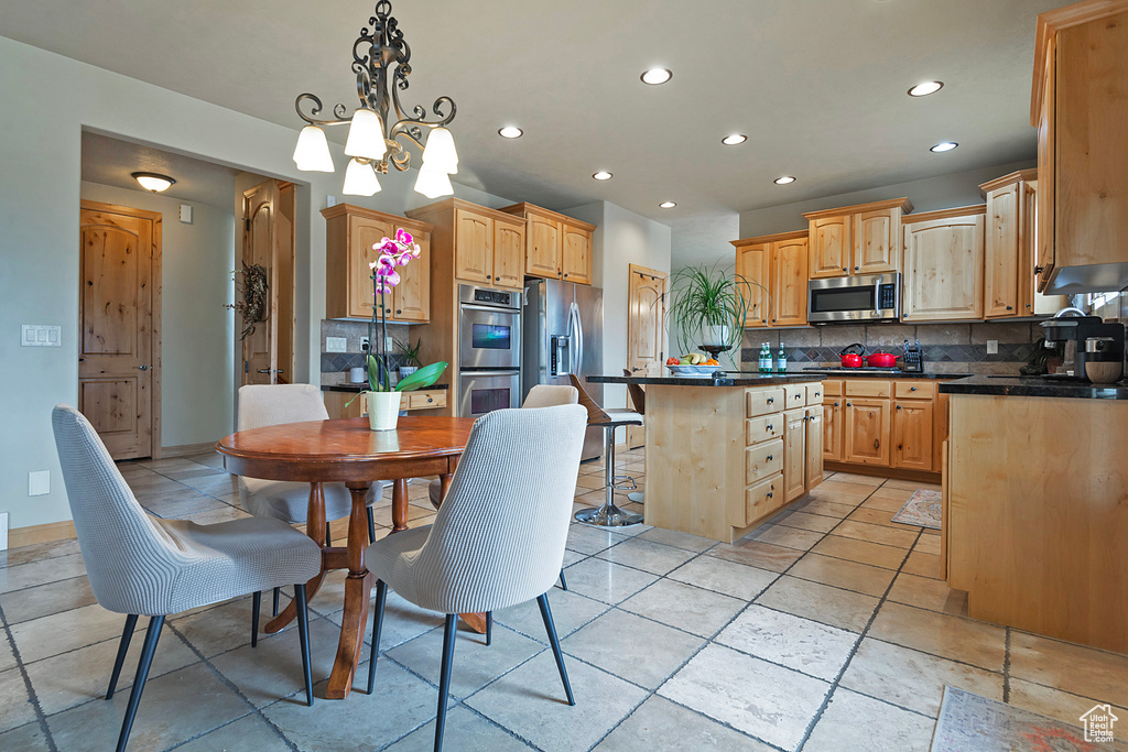 Kitchen featuring a kitchen breakfast bar, light tile flooring, stainless steel appliances, a notable chandelier, and tasteful backsplash