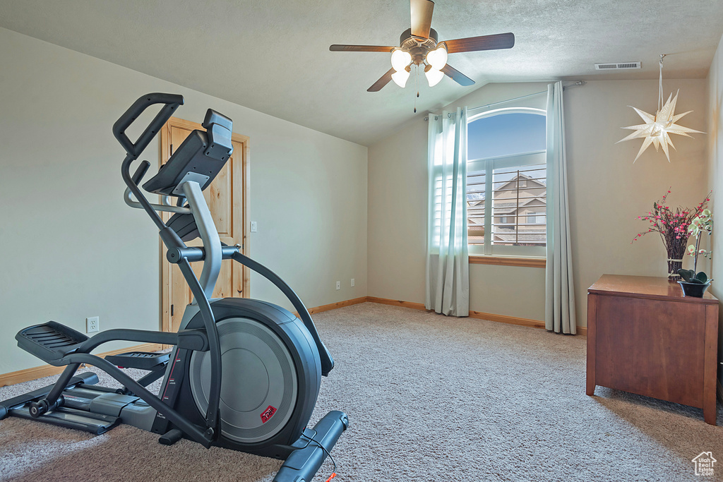 Exercise area featuring a textured ceiling, lofted ceiling, light carpet, and ceiling fan