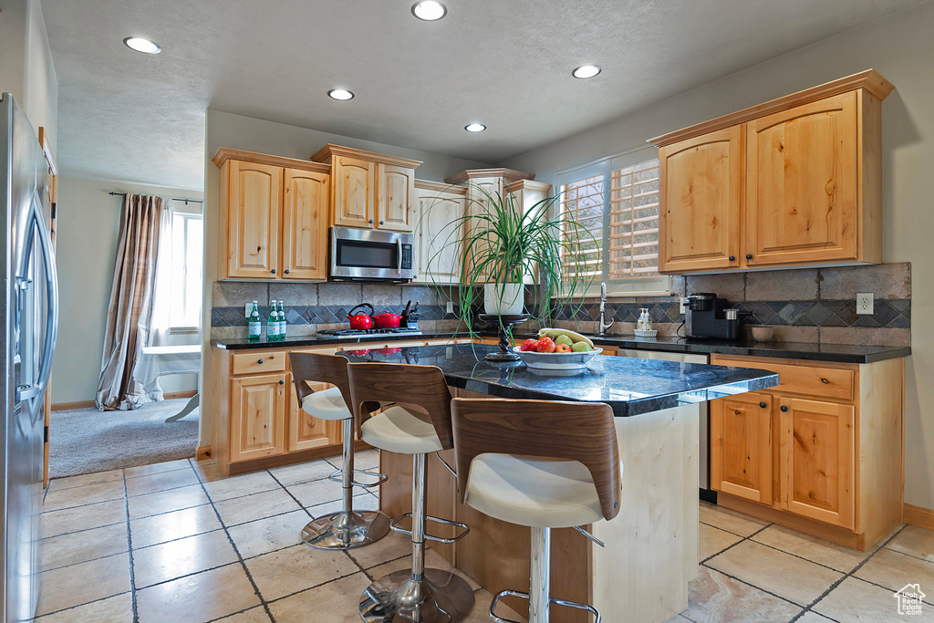 Kitchen with light tile floors, a kitchen island, stainless steel appliances, and backsplash