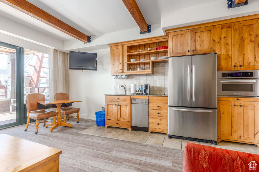 Kitchen with tasteful backsplash, beam ceiling, appliances with stainless steel finishes, and light tile floors