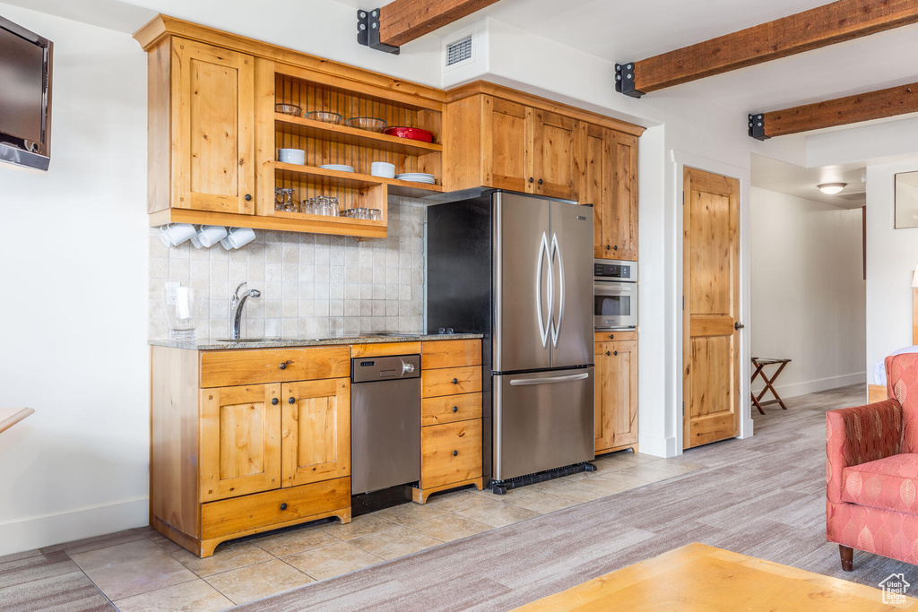 Kitchen with backsplash, sink, appliances with stainless steel finishes, light stone countertops, and beamed ceiling