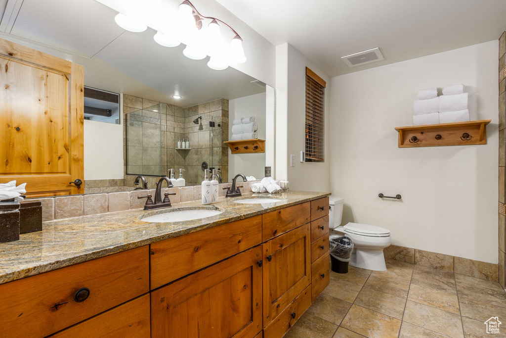 Bathroom with double sink, tile flooring, a tile shower, large vanity, and toilet