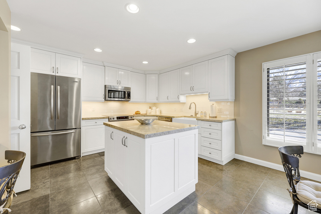 Kitchen featuring stainless steel appliances, white cabinets, tile floors, a center island, and tasteful backsplash