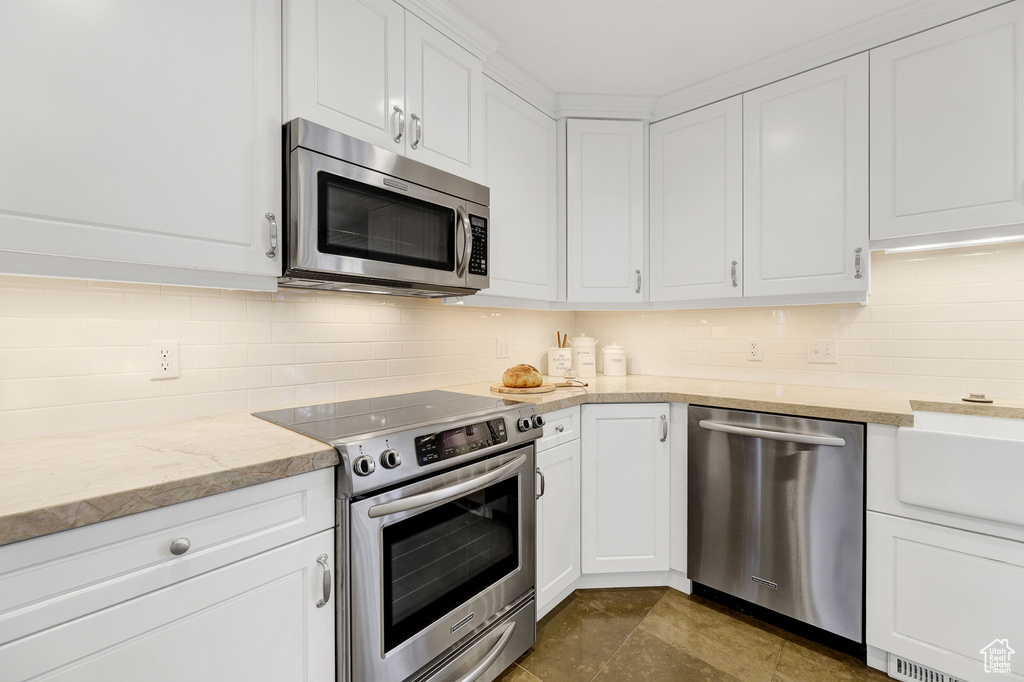 Kitchen featuring tasteful backsplash, stainless steel appliances, white cabinets, and light stone countertops