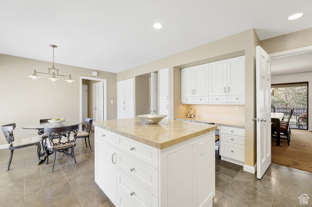 Kitchen featuring white cabinetry, decorative light fixtures, light stone countertops, a kitchen island, and light tile floors