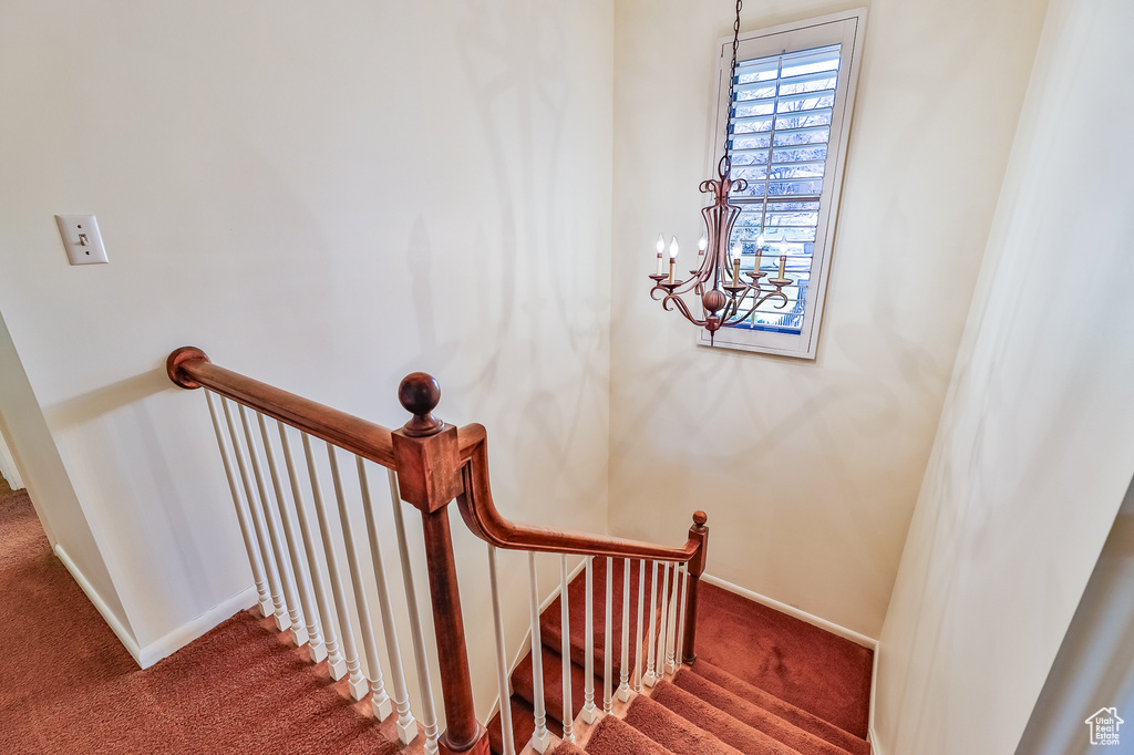 Staircase with dark carpet and an inviting chandelier
