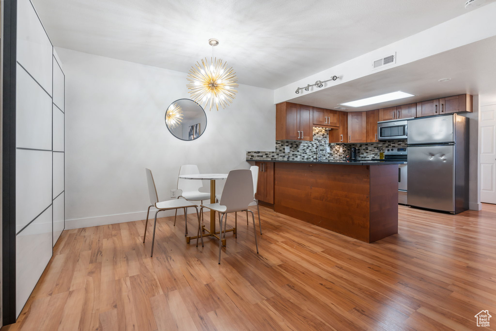 Kitchen featuring hanging light fixtures, kitchen peninsula, light hardwood / wood-style floors, stainless steel appliances, and a chandelier