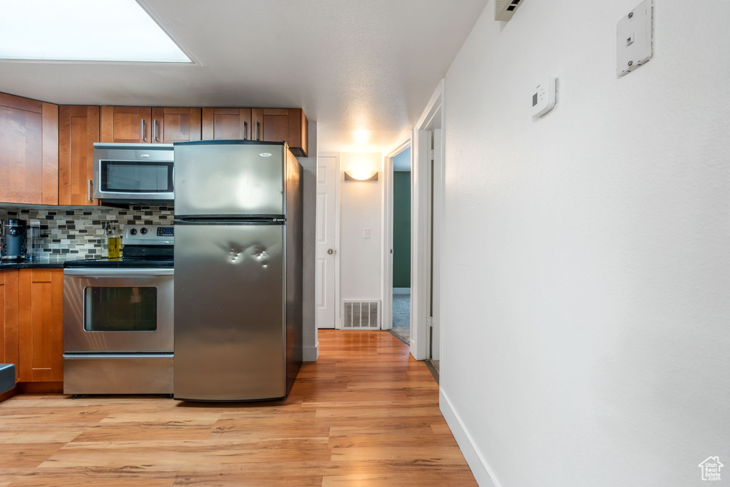 Kitchen featuring backsplash, a skylight, light wood-type flooring, and stainless steel appliances