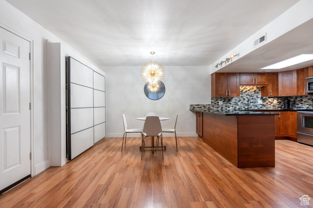 Kitchen with pendant lighting, range, tasteful backsplash, a chandelier, and light wood-type flooring